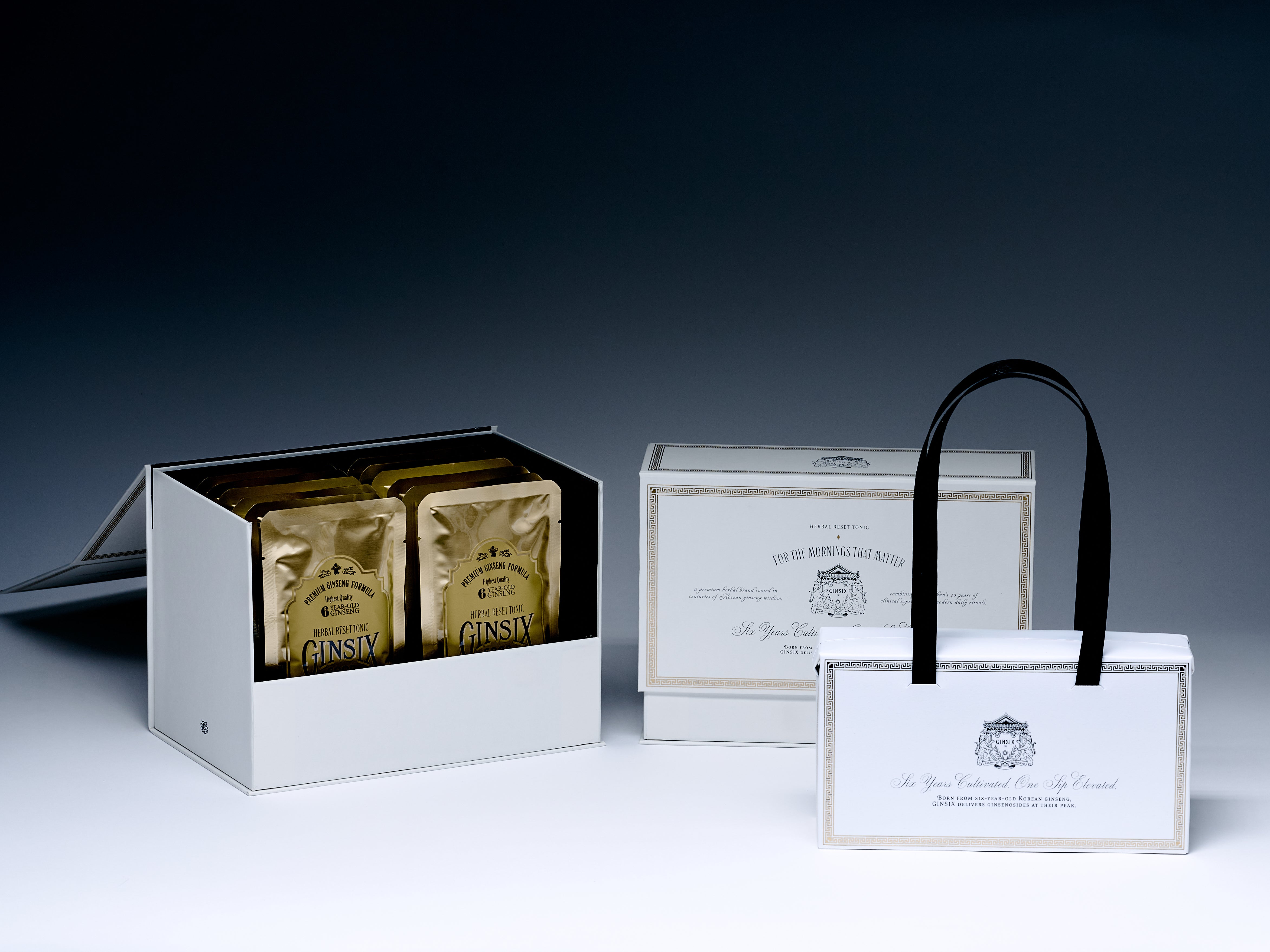 GINSIX gift box open with gold tonic pouches beside two closed boxes with ribbon handle